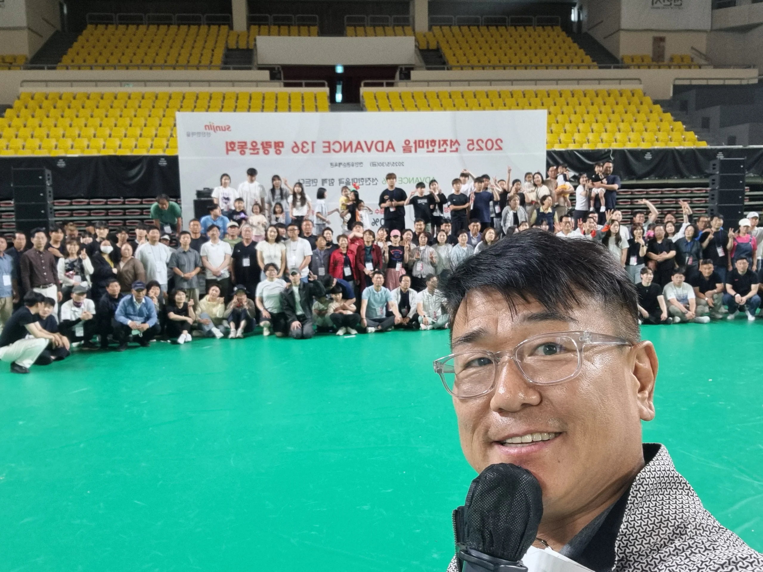 실내 체육관 관중석에 앉은 참가자들 앞에서 마이크를 든 진행자