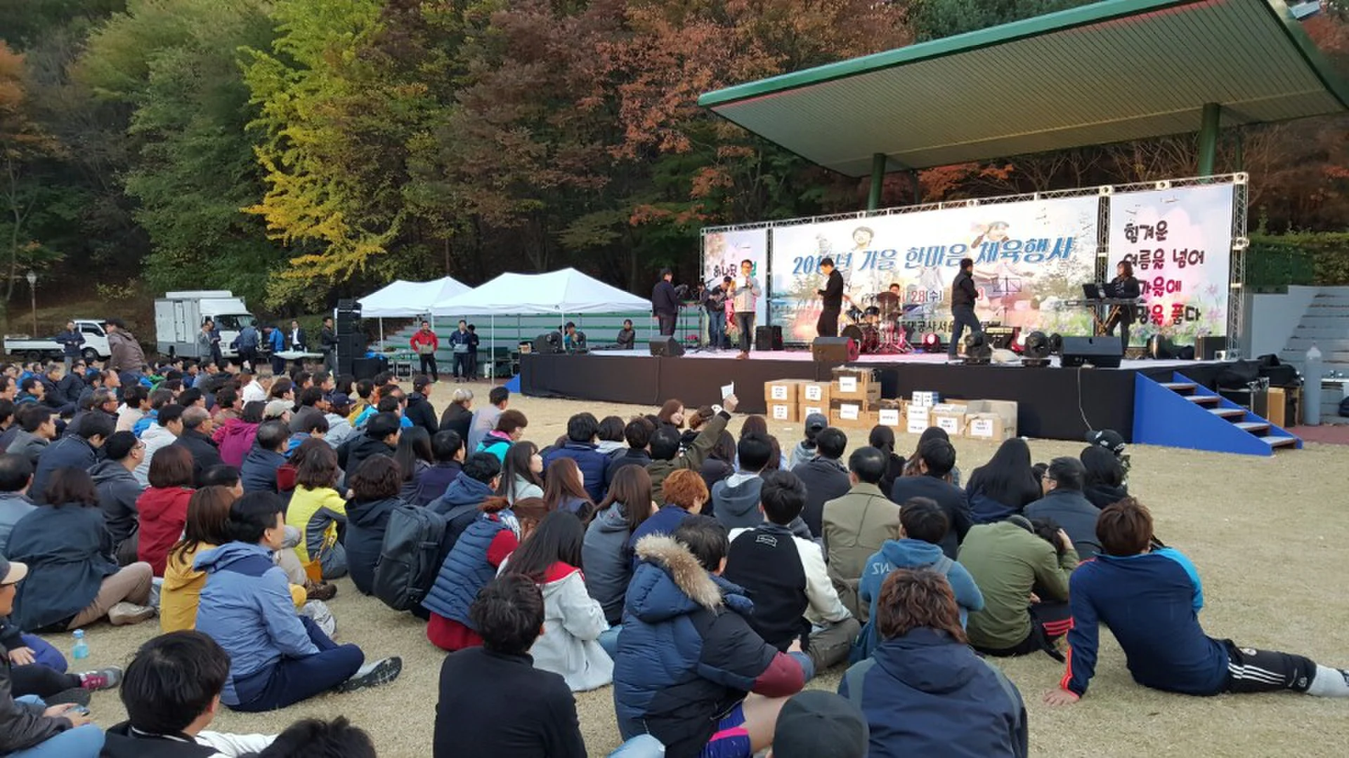 야외 무대를 바라보며 앉아 있는 참가자들을 멀리서 담은 모습