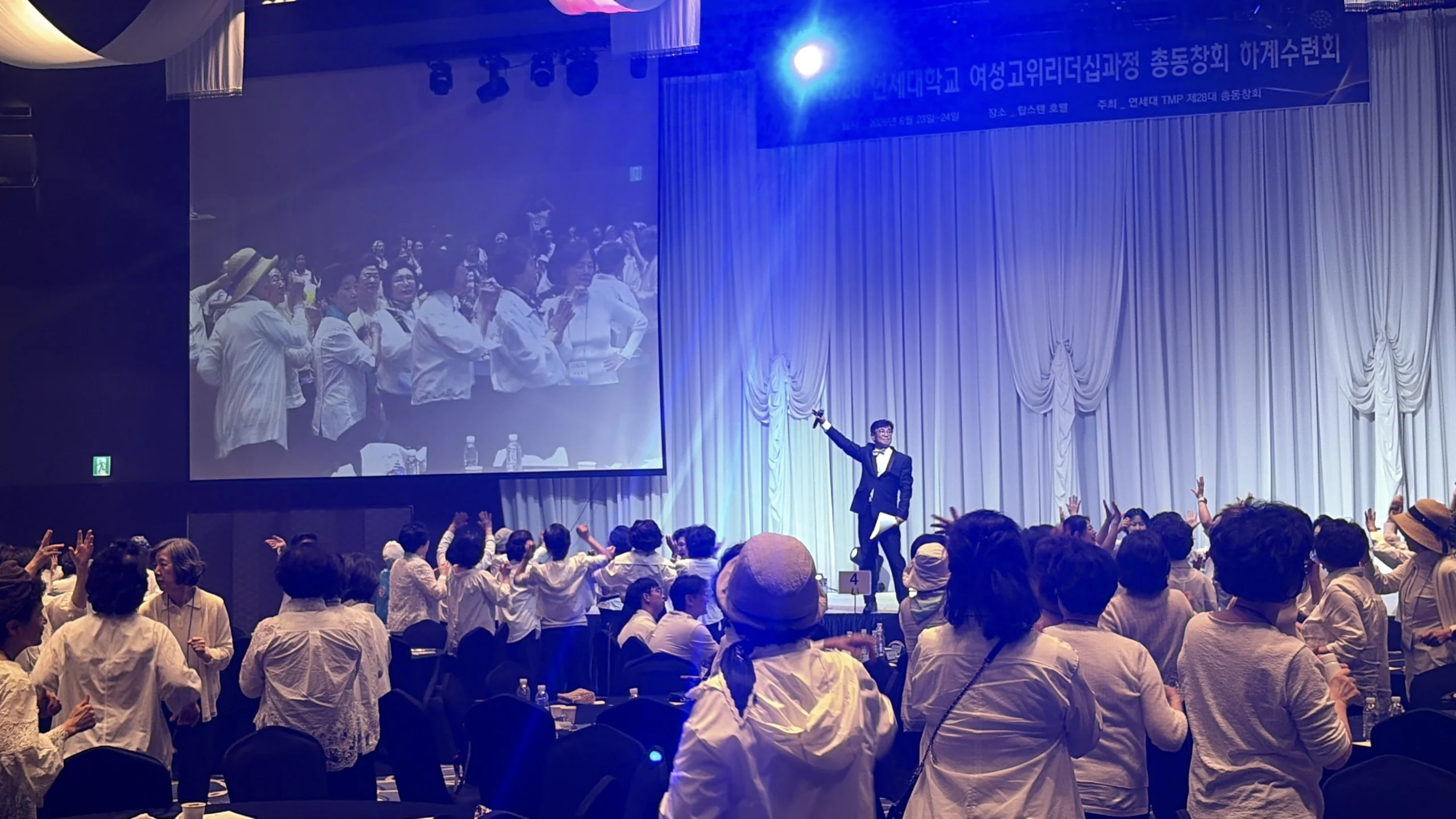 실내 무대에서 대형 스크린을 배경으로 선 채 모여 있는 참가자들