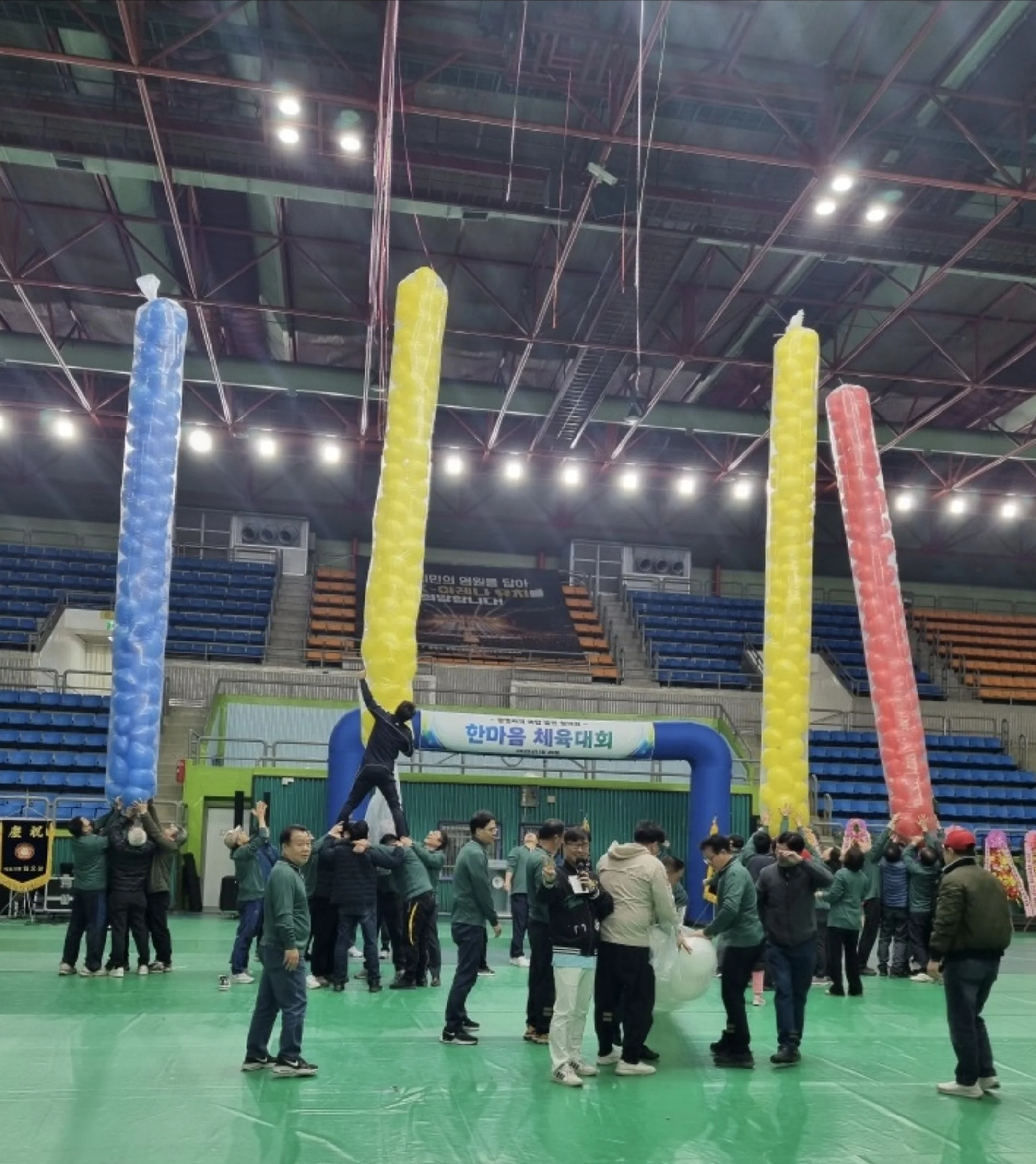 경기장 풍선 기둥 사이로 초록색 단체복을 입은 그룹이 중앙에 모인 모습