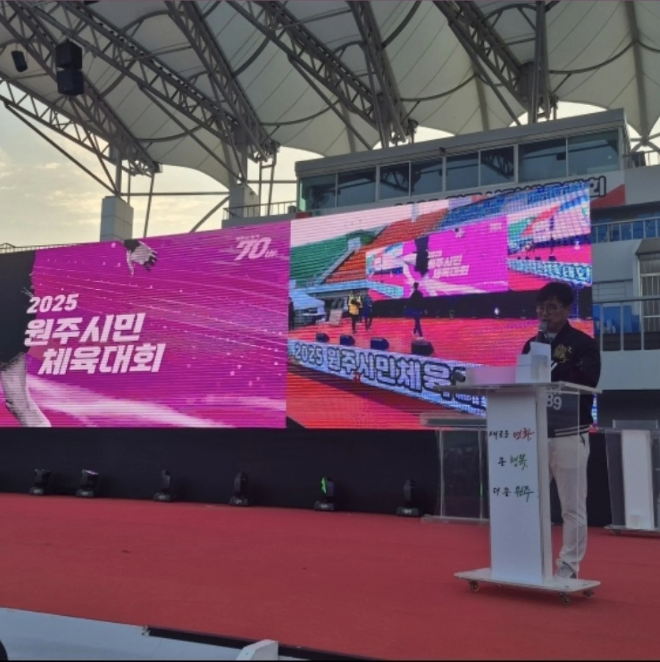 분홍빛 조명이 비치는 무대에 체육대회 현수막이 걸린 모습