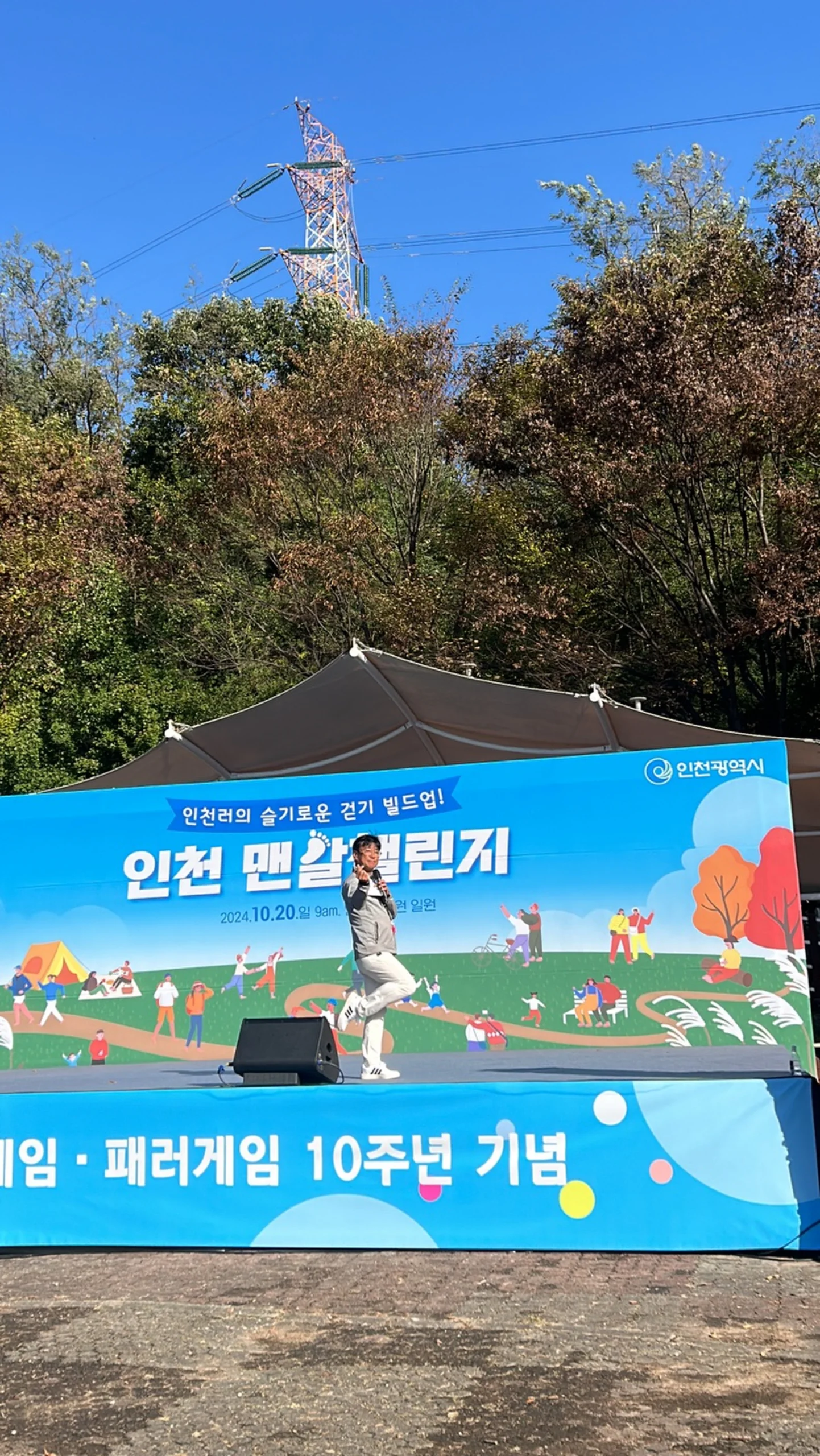야외 무대 현수막을 배경으로 진행 중인 사회자를 먼 거리에서 담은 모습