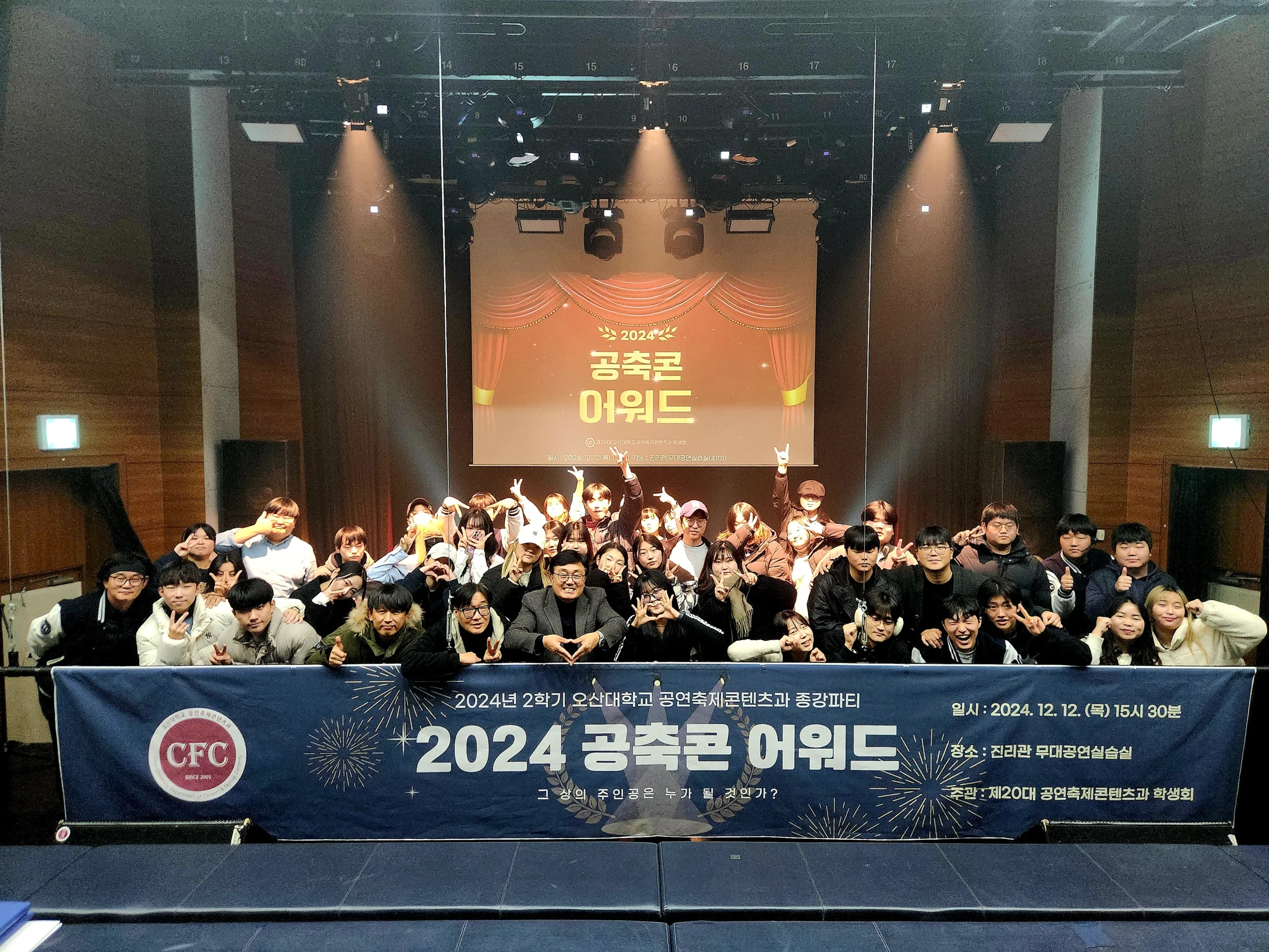 스크린이 설치된 실내 행사장 무대와 앉아 있는 참가자들