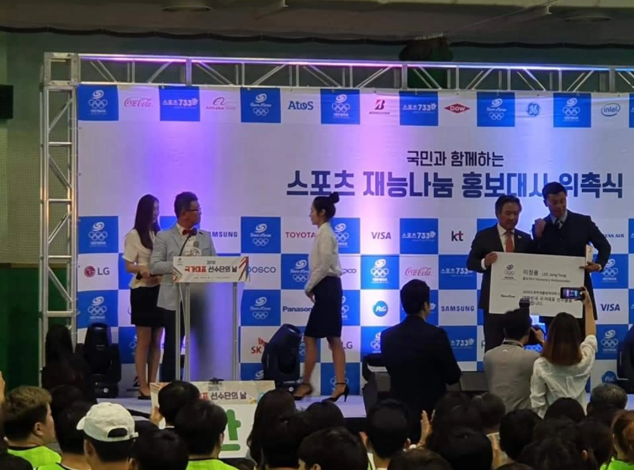 현수막이 걸린 실내 체육관에 앉은 관중과 단상이 보이는 전경