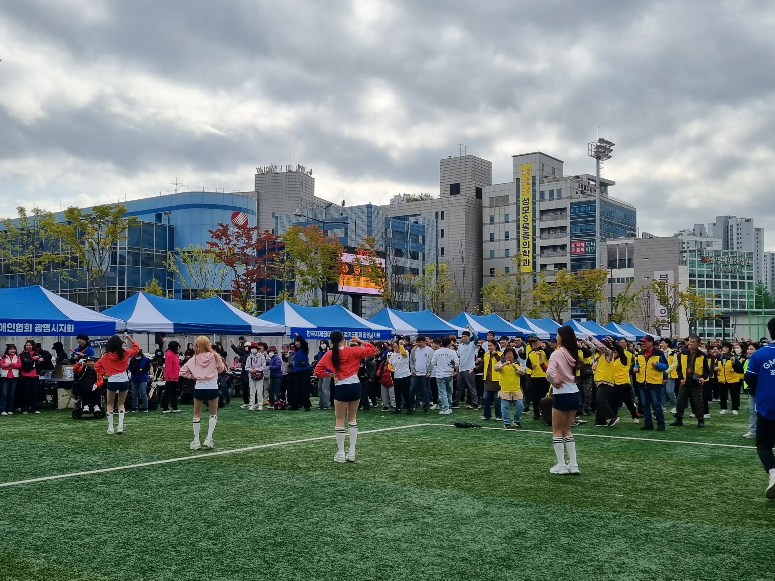 텐트가 늘어선 도심 야외 운동장과 멀리 모인 참가자들 전경