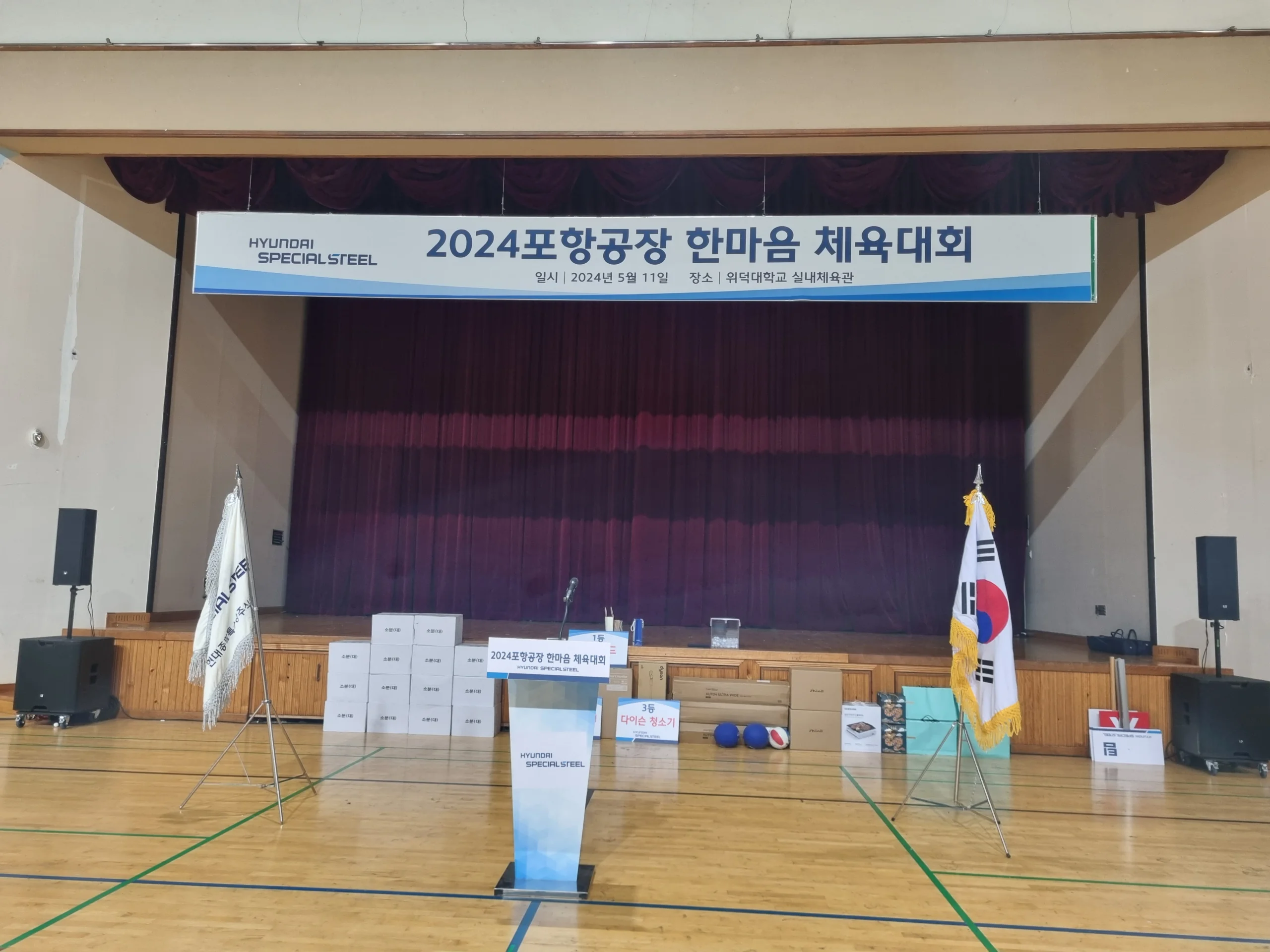 실내 체육관 무대에 단상과 현수막이 설치된 공식 행사 준비 모습