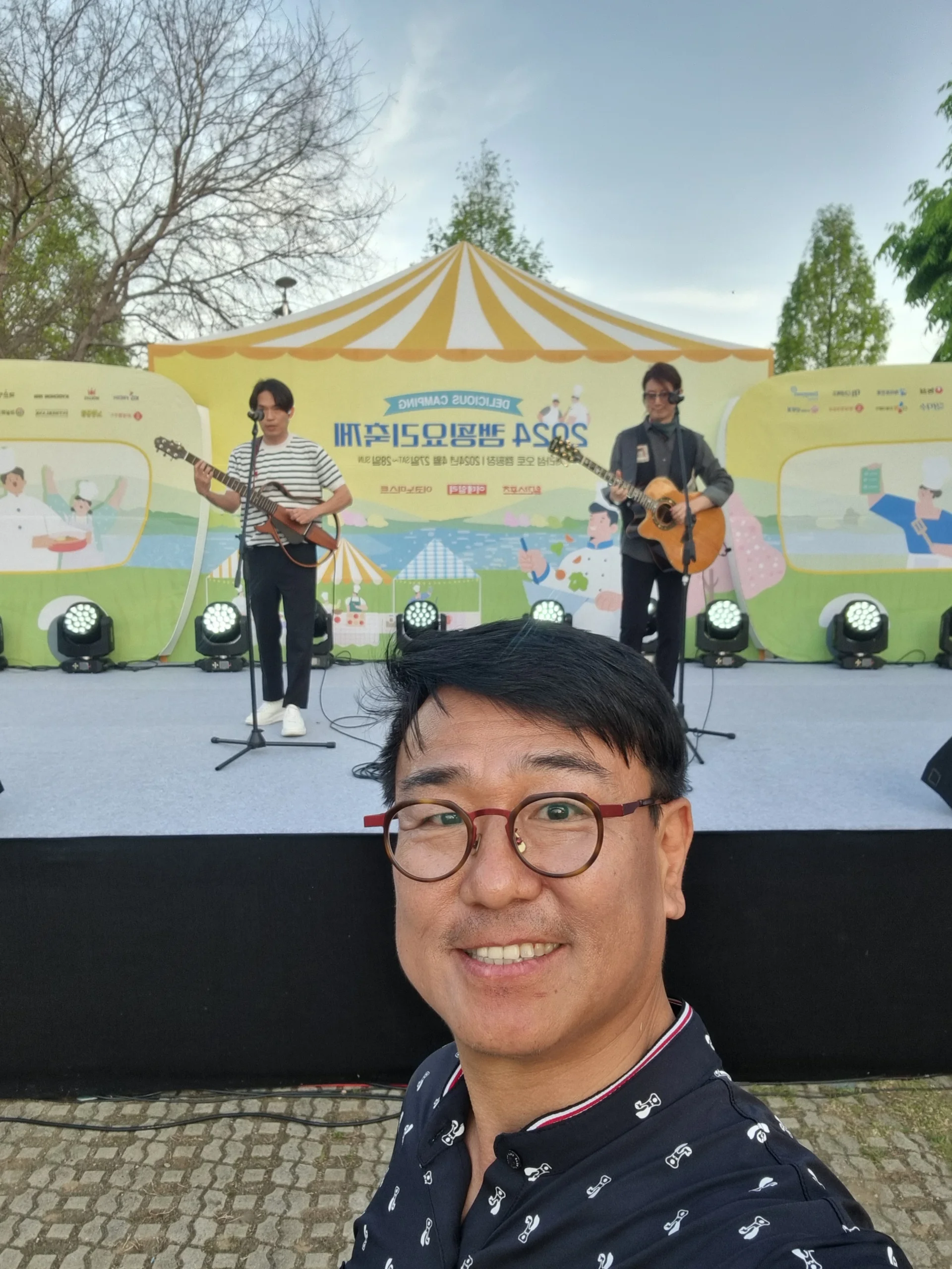야외 축제 무대에서 밴드와 천막을 배경으로 넓게 담은 모습