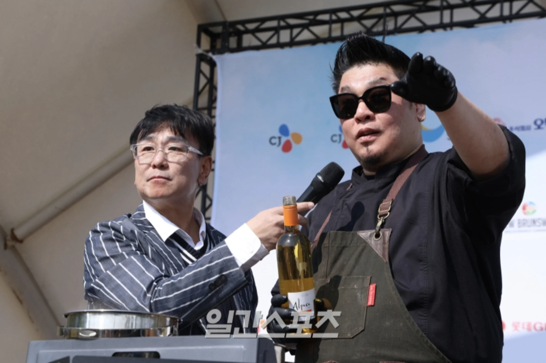 야외 무대에서 대형 스크린을 배경으로 마이크와 생수병을 든 진행자